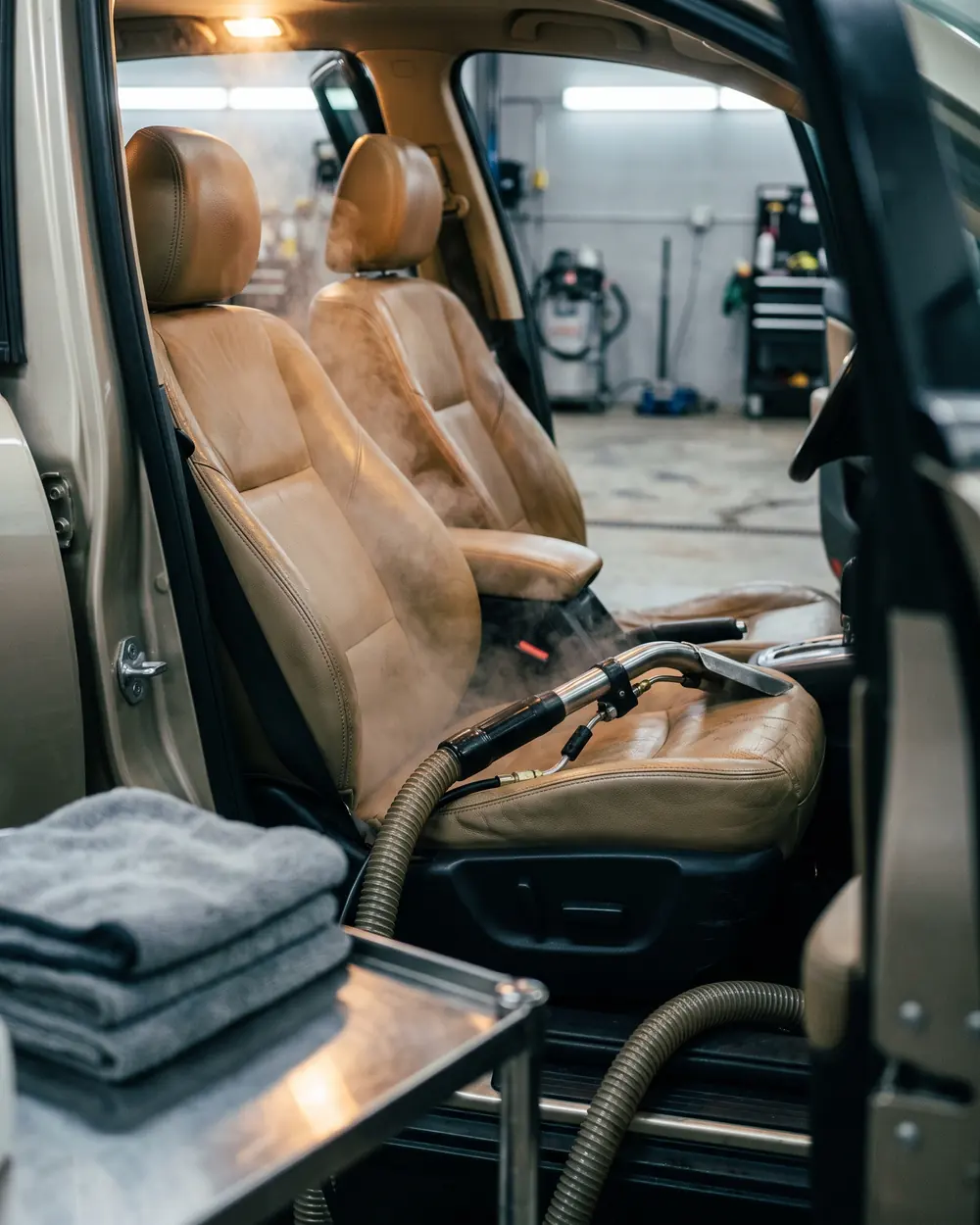 A tan leather seat just steamed, a steam wand resting on its bolster, folded towels on a cart in front.